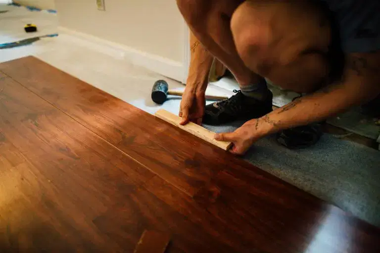 Person installing dark wood laminate flooring indoors using a tapping block during home renovation work