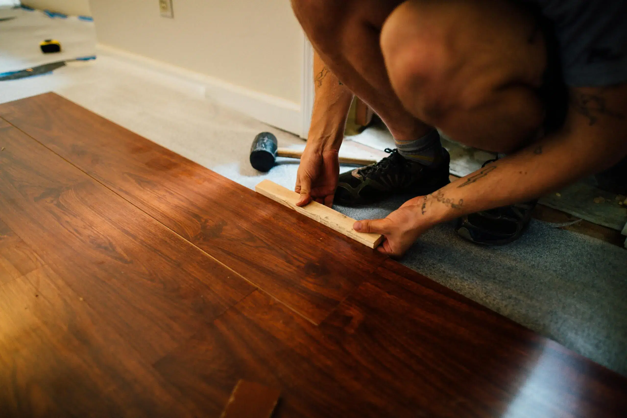 Person installing dark wood laminate flooring indoors using a tapping block during home renovation work